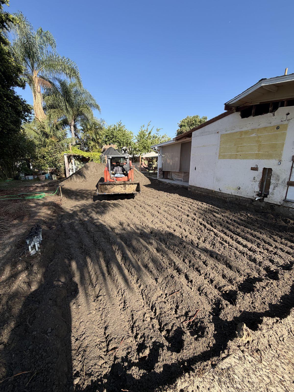 Skid steer grading and compacting soil to prepare an ADU building pad