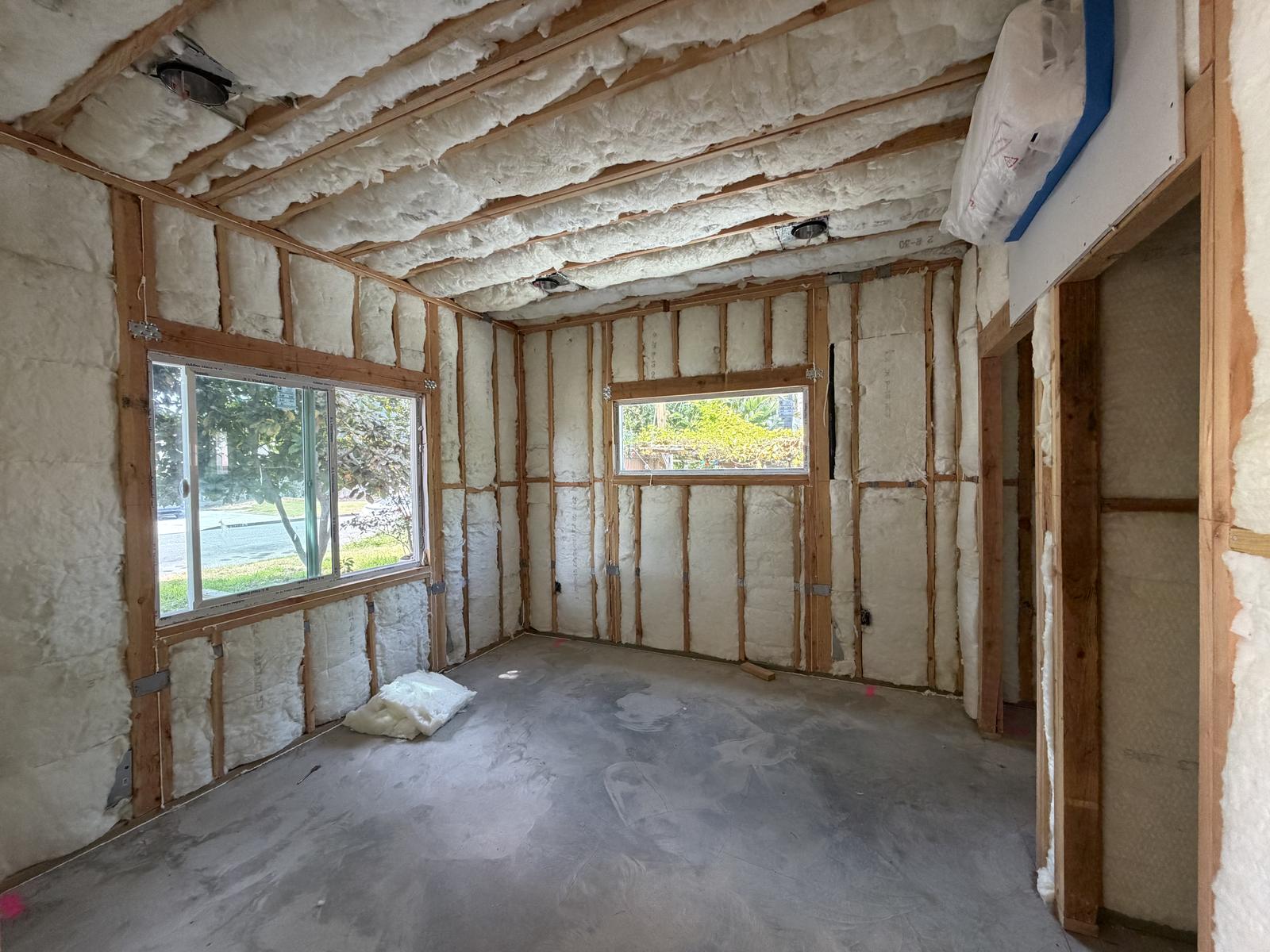 Insulated ADU room with spray foam ceiling and batt wall insulation and a doorway to an adjoining room