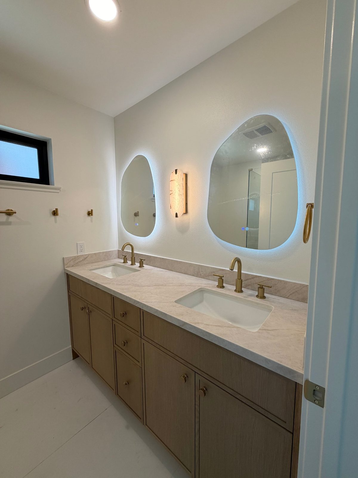 Double vanity bathroom with backlit organic-shaped mirrors and brushed gold fixtures