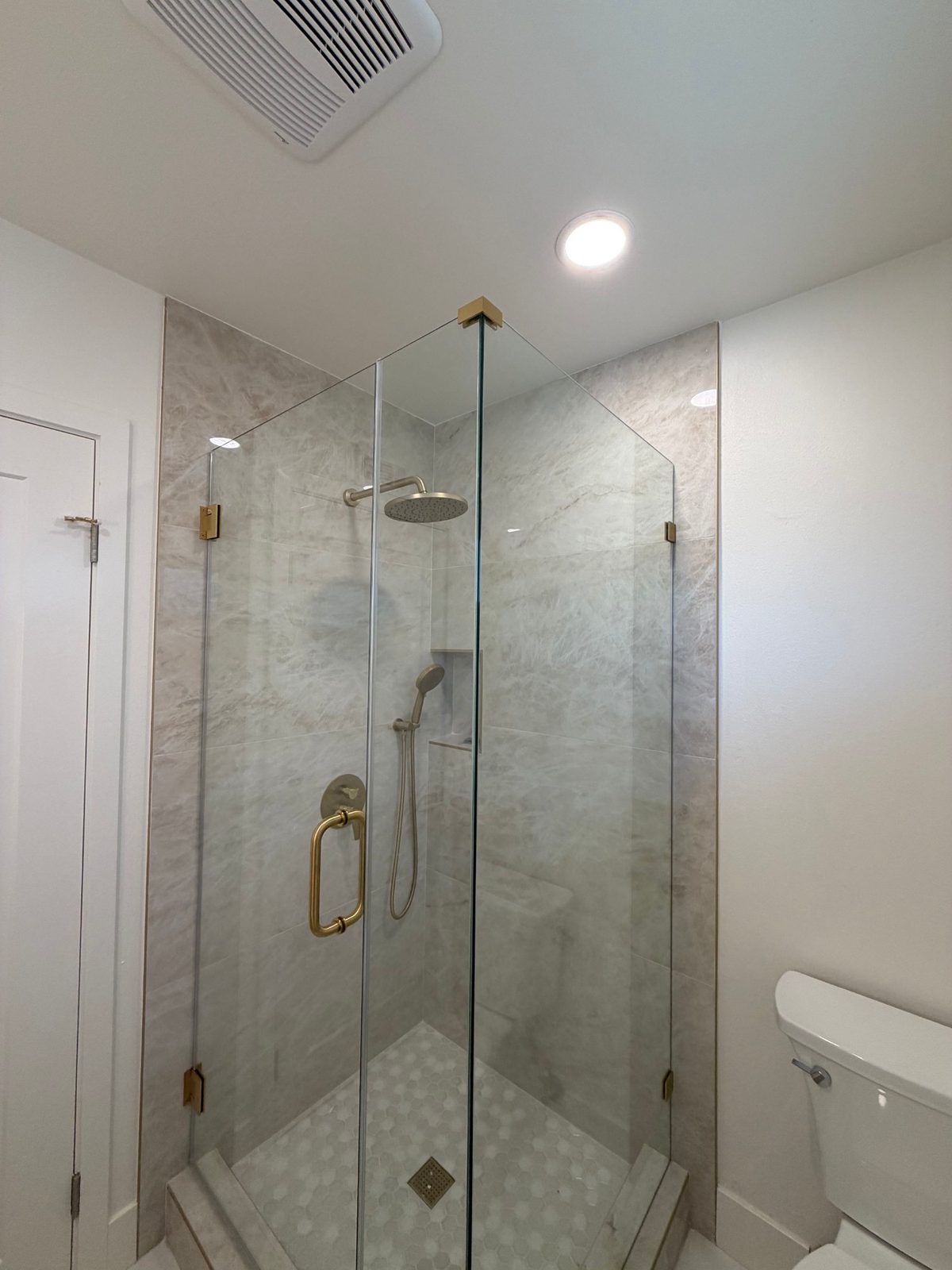 Corner glass shower with marble-look tile and brushed gold hardware