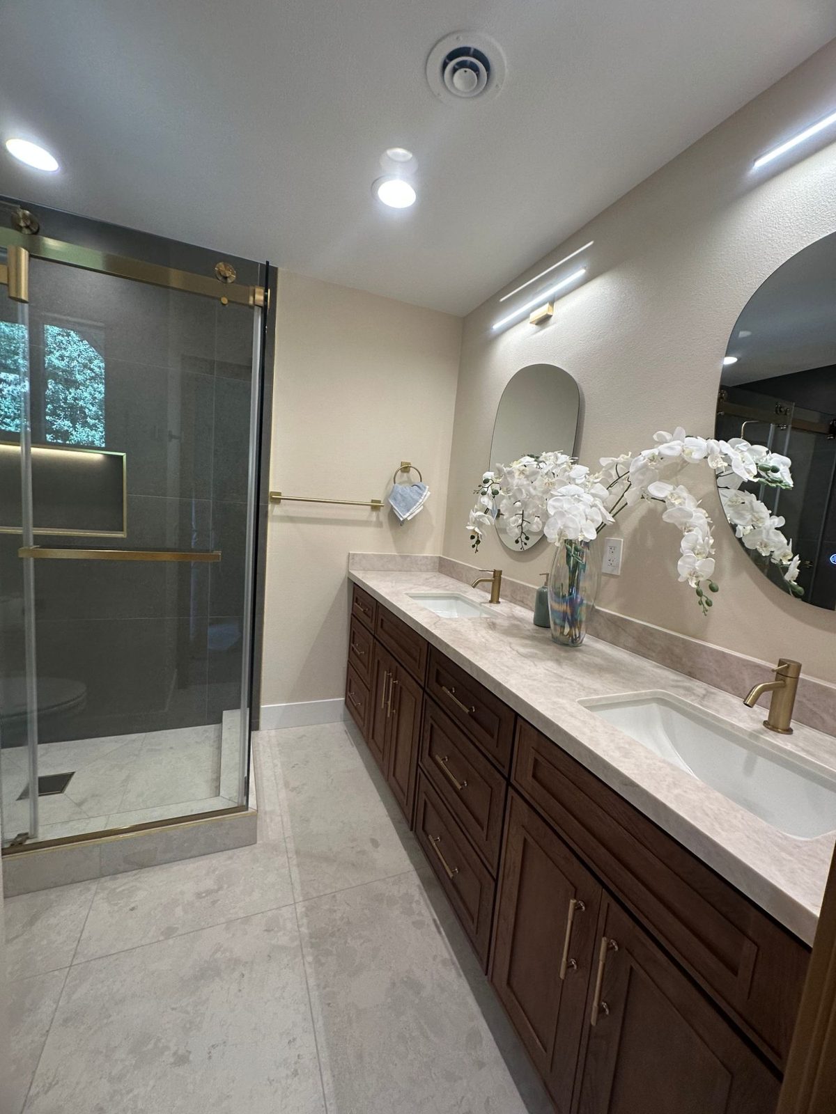 Double vanity bathroom with dark wood cabinetry, round mirrors, and walk-in glass shower