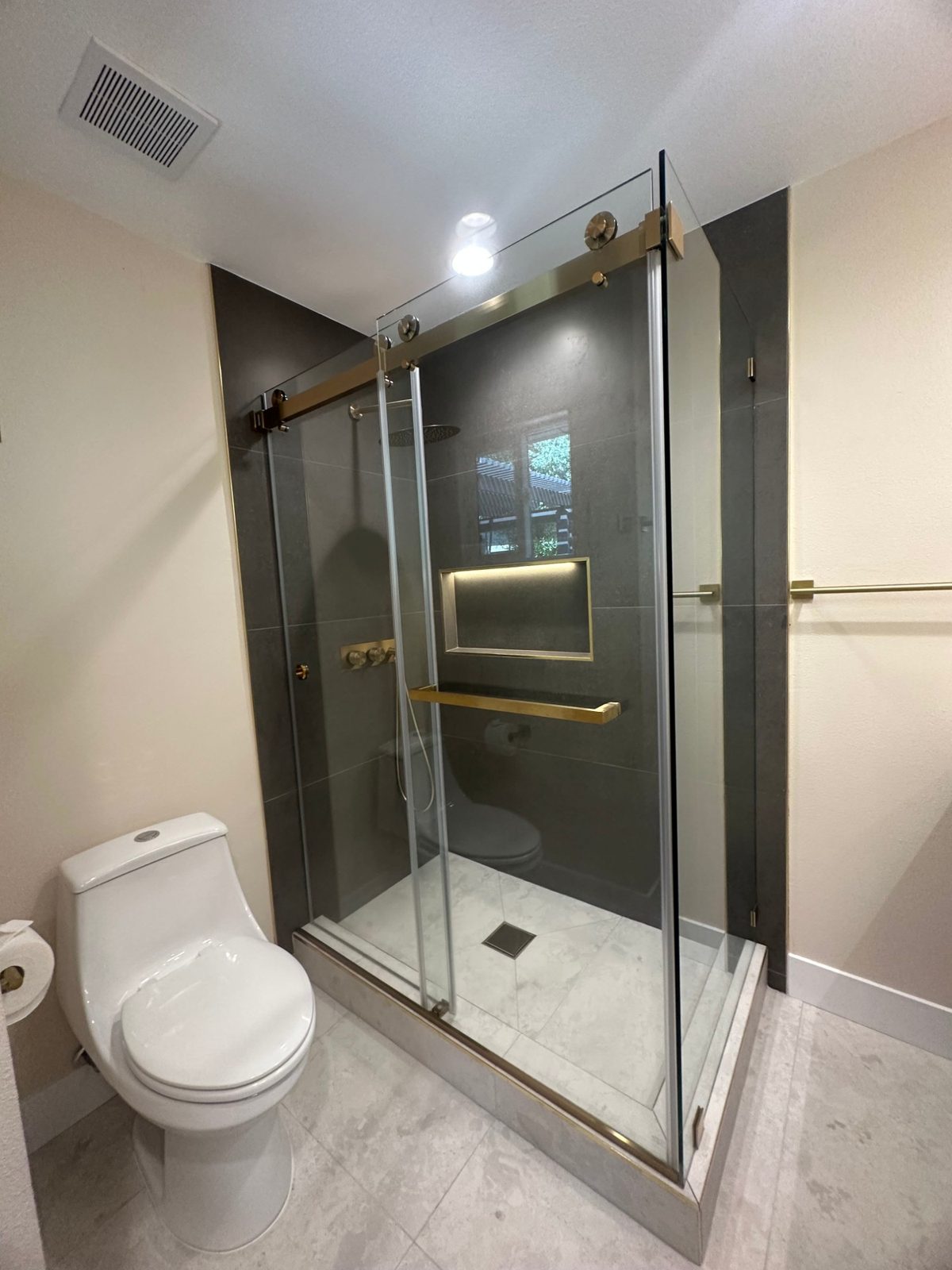 Sliding glass shower door with gold hardware and dark tile shower surround