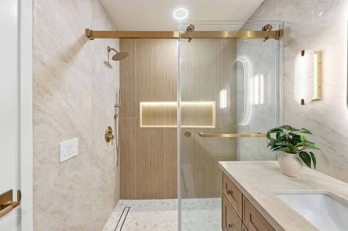 Walk-in glass shower with brushed gold hardware, wood-look tile accent wall, and marble surround