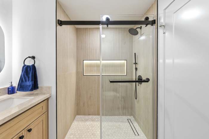 Walk-in glass shower with matte black hardware and wood-look tile accent wall