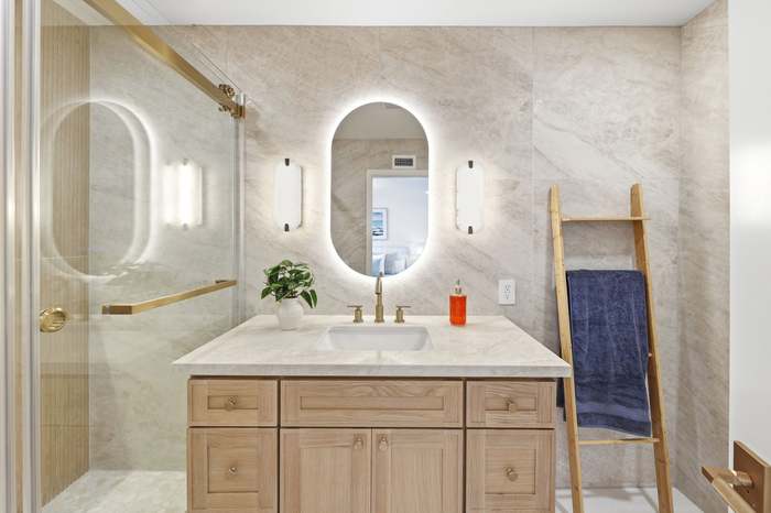 Bathroom vanity with backlit oval mirror, marble walls, and wood ladder towel rack