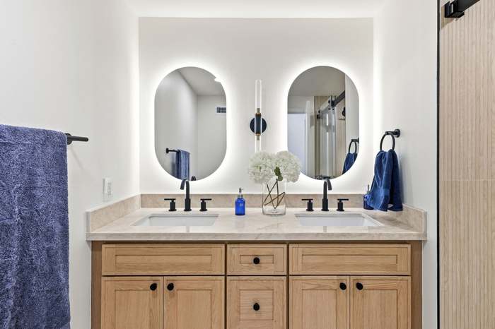 Double vanity bathroom with backlit oval mirrors and matte black fixtures