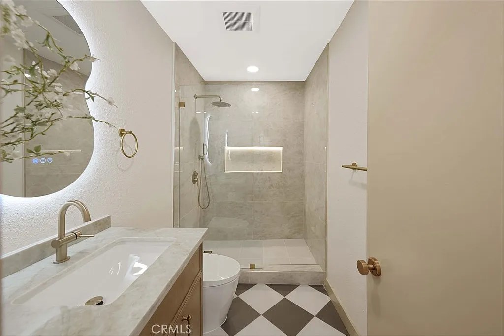 Walk-in glass shower with checkerboard tile floor, brushed gold rain shower head, and marble tile surround