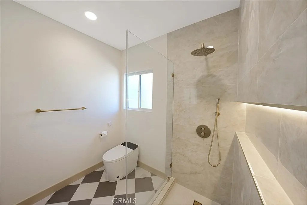 Corner glass shower with checkerboard tile floor, marble surround, and brushed gold fixtures