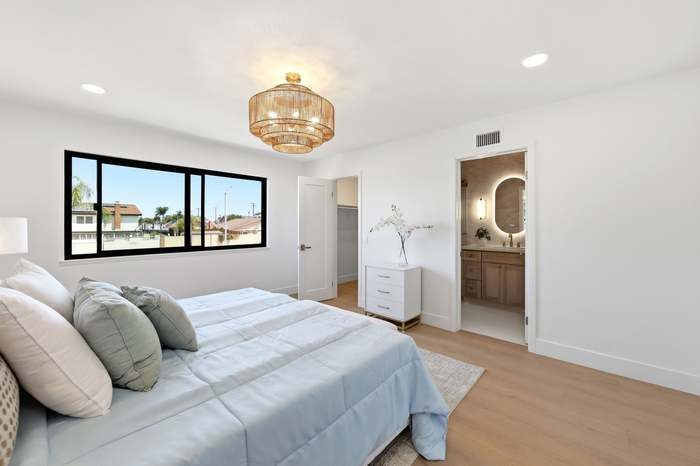 Primary bedroom with blue bedding, gold beaded chandelier, walk-in closet, and ensuite bathroom