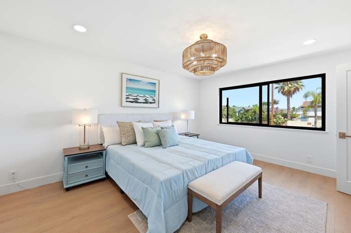 Staged bedroom with ocean-view window, blue bedding, and a beach-themed art print