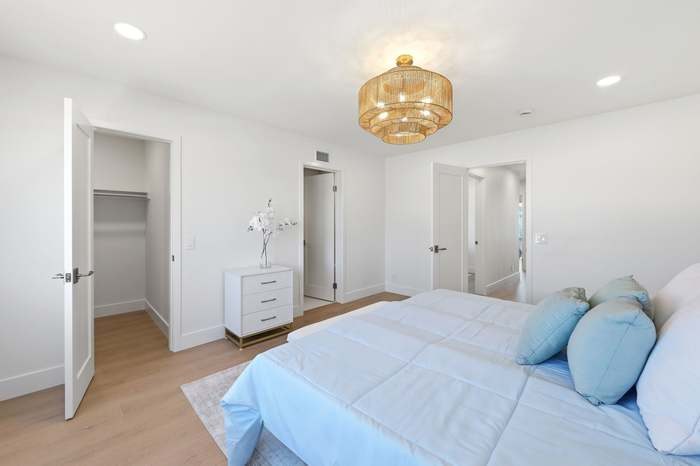 Bedroom with open walk-in closet, white dresser, and gold beaded chandelier