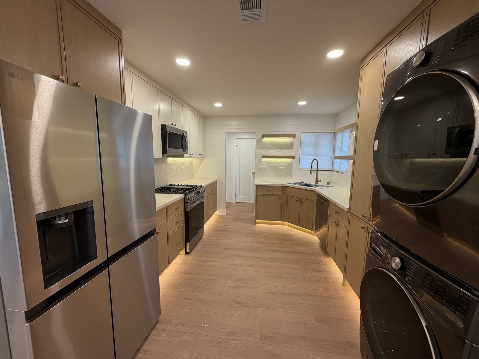 Galley kitchen with stainless steel refrigerator, light wood and white cabinetry, and a gas range