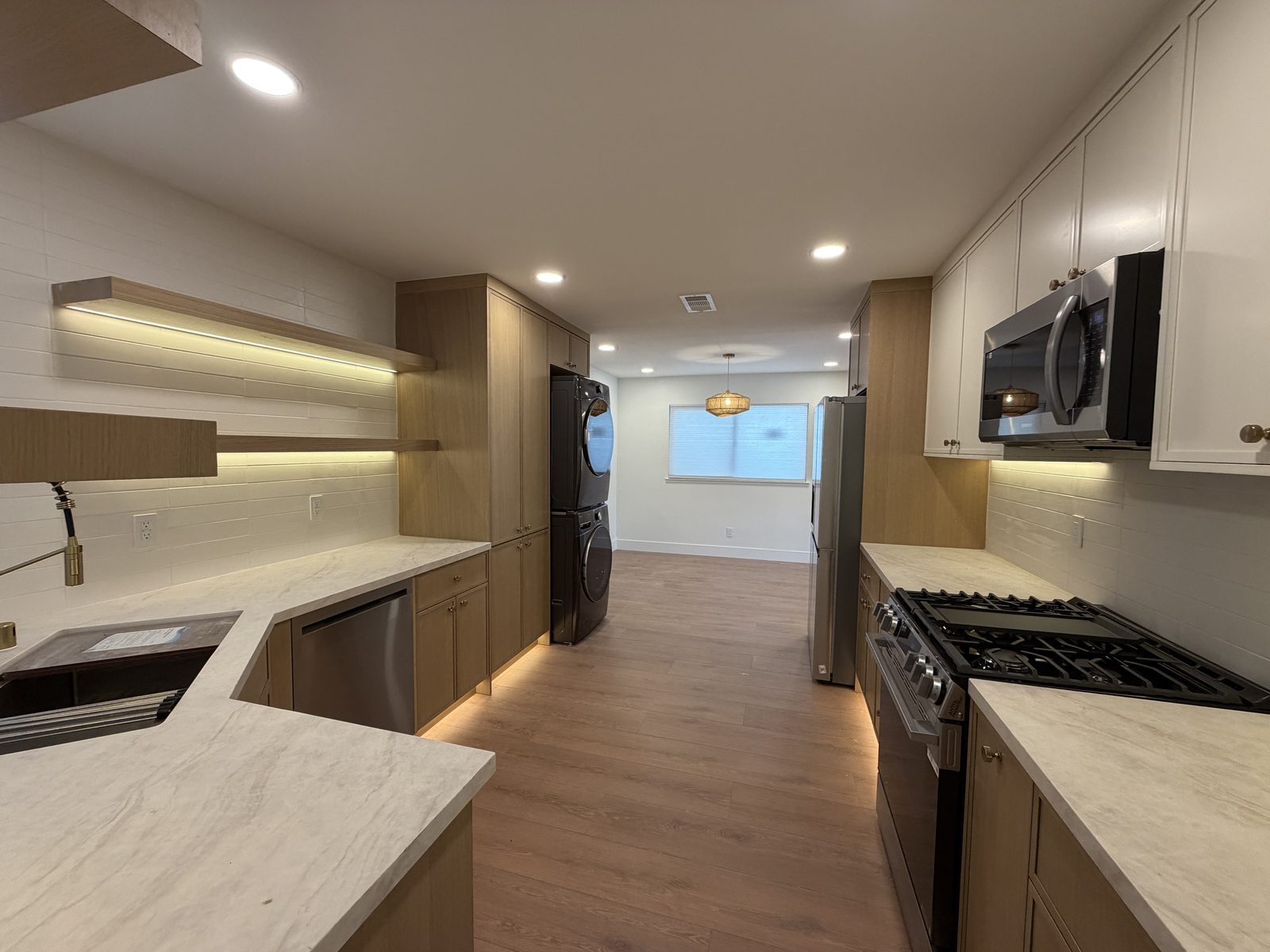 Light wood kitchen with floating shelves, gas cooktop, and white upper cabinets