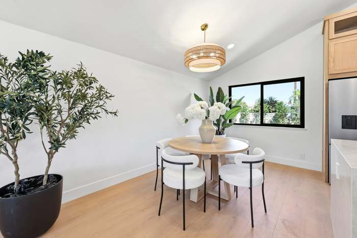 Open-concept dining nook with round wood table, wire-frame chairs, and a beaded chandelier next to the kitchen
