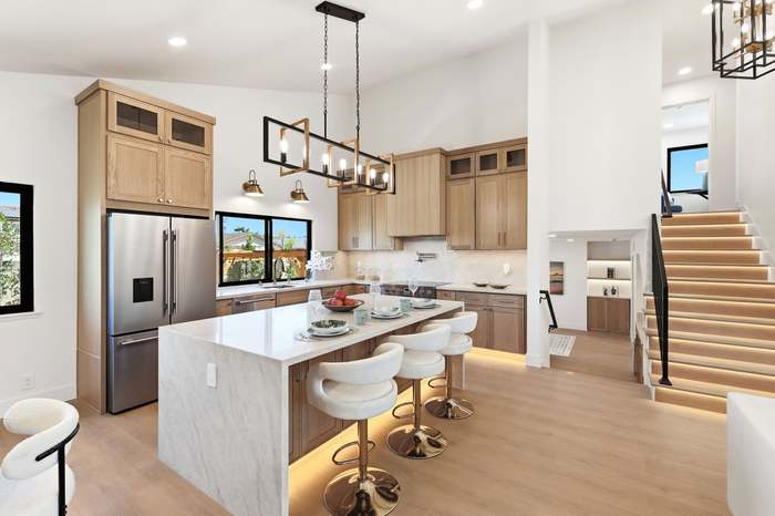 Light wood kitchen with waterfall island, gold barstools, and a linear chandelier under a vaulted ceiling