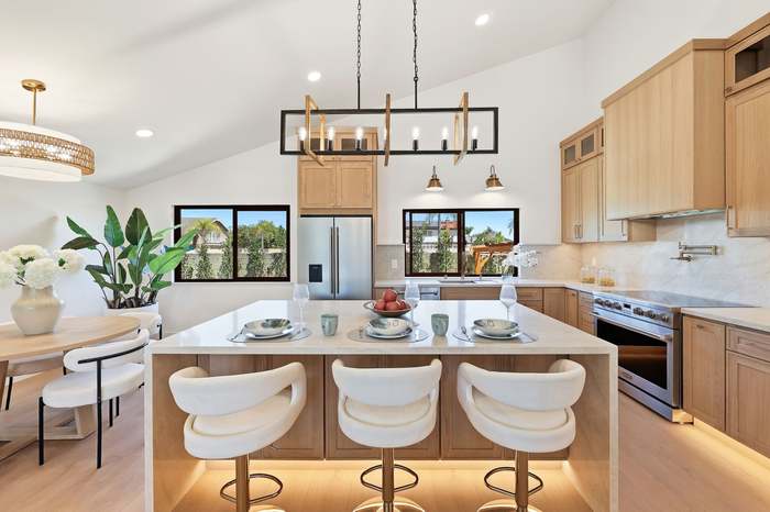 Light wood kitchen with vaulted ceiling, pot filler, and a marble waterfall island set for dinner
