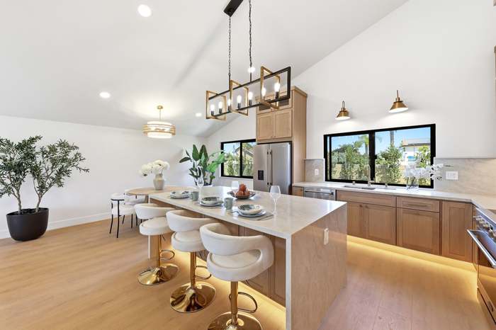 Light wood kitchen with marble island, gold barstools, and windows looking out to the backyard