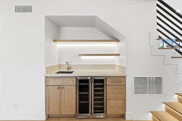 Built-in wet bar with wine fridge, marble backsplash, and floating wood shelves next to a staircase