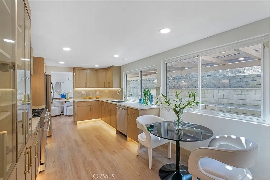 Galley kitchen with light wood cabinetry, marble backsplash, and a round breakfast table by a picture window