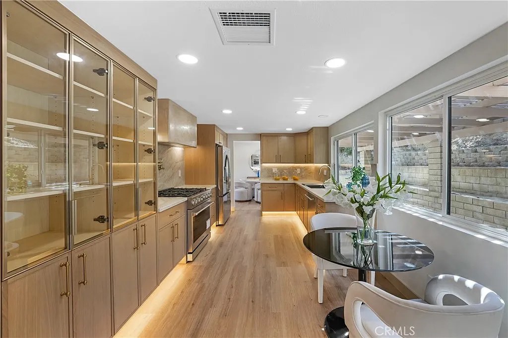 Galley kitchen with glass-front cabinetry, stainless range, and light wood flooring