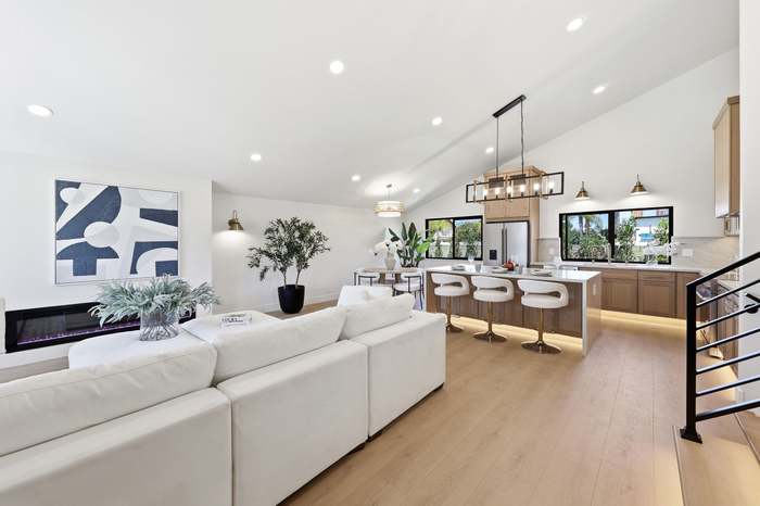 Open-concept living room with white sectional sofa, vaulted ceiling, and view into a kitchen with waterfall island