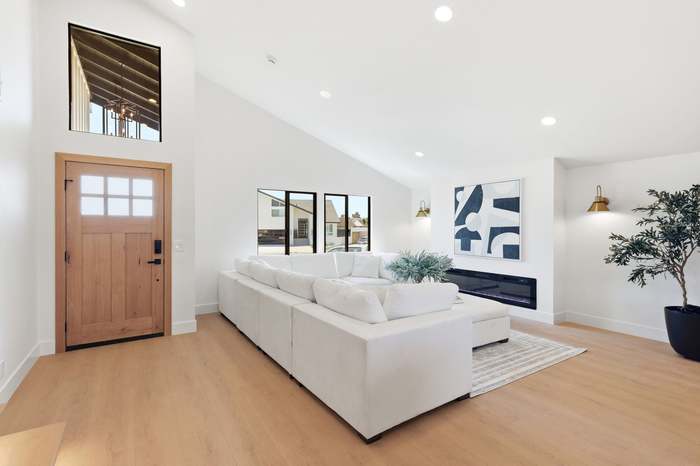 Living room entry with wood front door, white sectional sofa, and abstract art above a linear fireplace