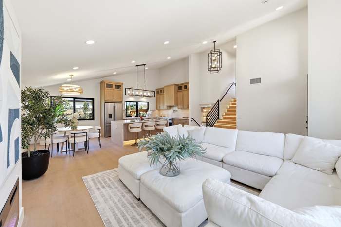 Open-concept living room with white sectional and ottoman, staircase with cable railing, and view into the kitchen and dining area