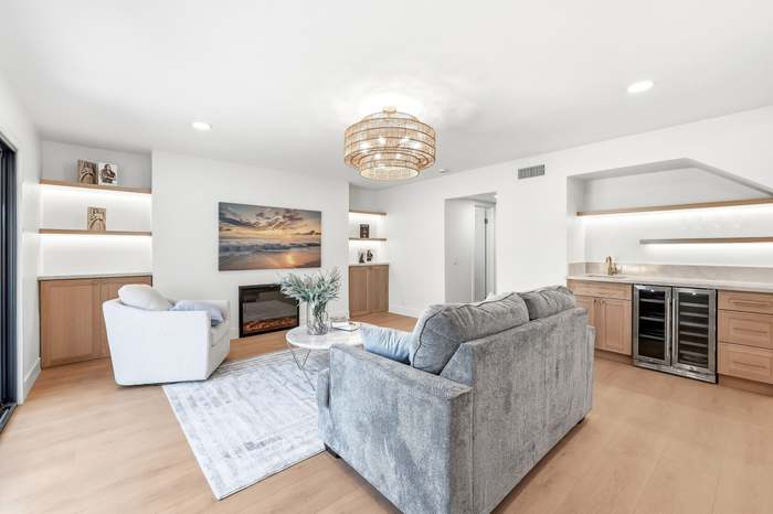 Living room with gray sectional, built-in shelving, wine fridge, and a beach sunset art print above the fireplace