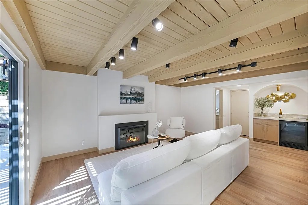 Living room with exposed wood beam ceiling, white sectional, linear fireplace, and an arched wet bar niche with wine fridge