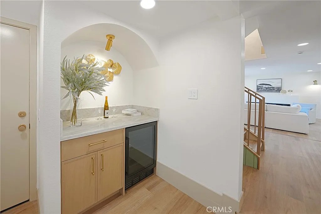 Built-in wet bar nook with wine fridge, marble countertop, and brushed gold sconce